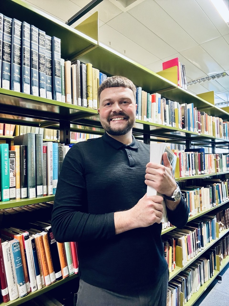 Professor Yan Kapranov standing among bookshelves in an academic library